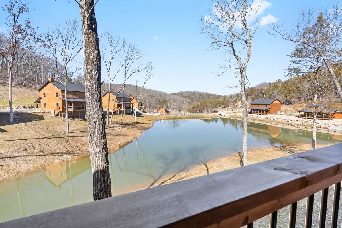 A beautiful wide-angle view of a pond surrounded by cozy cabins and trees, with distant mountains in the background. The lighting suggests either sunrise or sunset, and the mood is calm and serene—ideal for lakeside strolls or quiet moments.