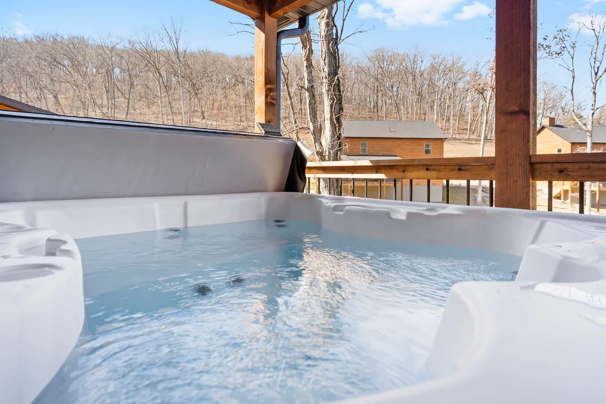 A secluded hot tub set among tall trees, with distant houses barely visible through the foliage. The mood is serene, offering a private nook for relaxation, stargazing, or enjoying a coffee surrounded by nature.