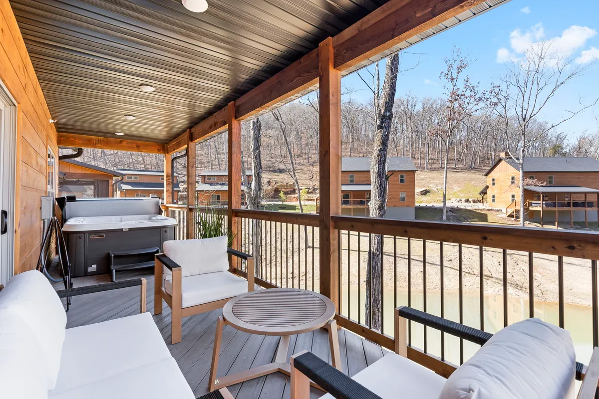 A tranquil outdoor hot tub with a seating area, positioned to overlook a scenic view of the water. The setting is serene, with lush greenery and the shimmering water providing an intimate, relaxing atmosphere perfect for couples.