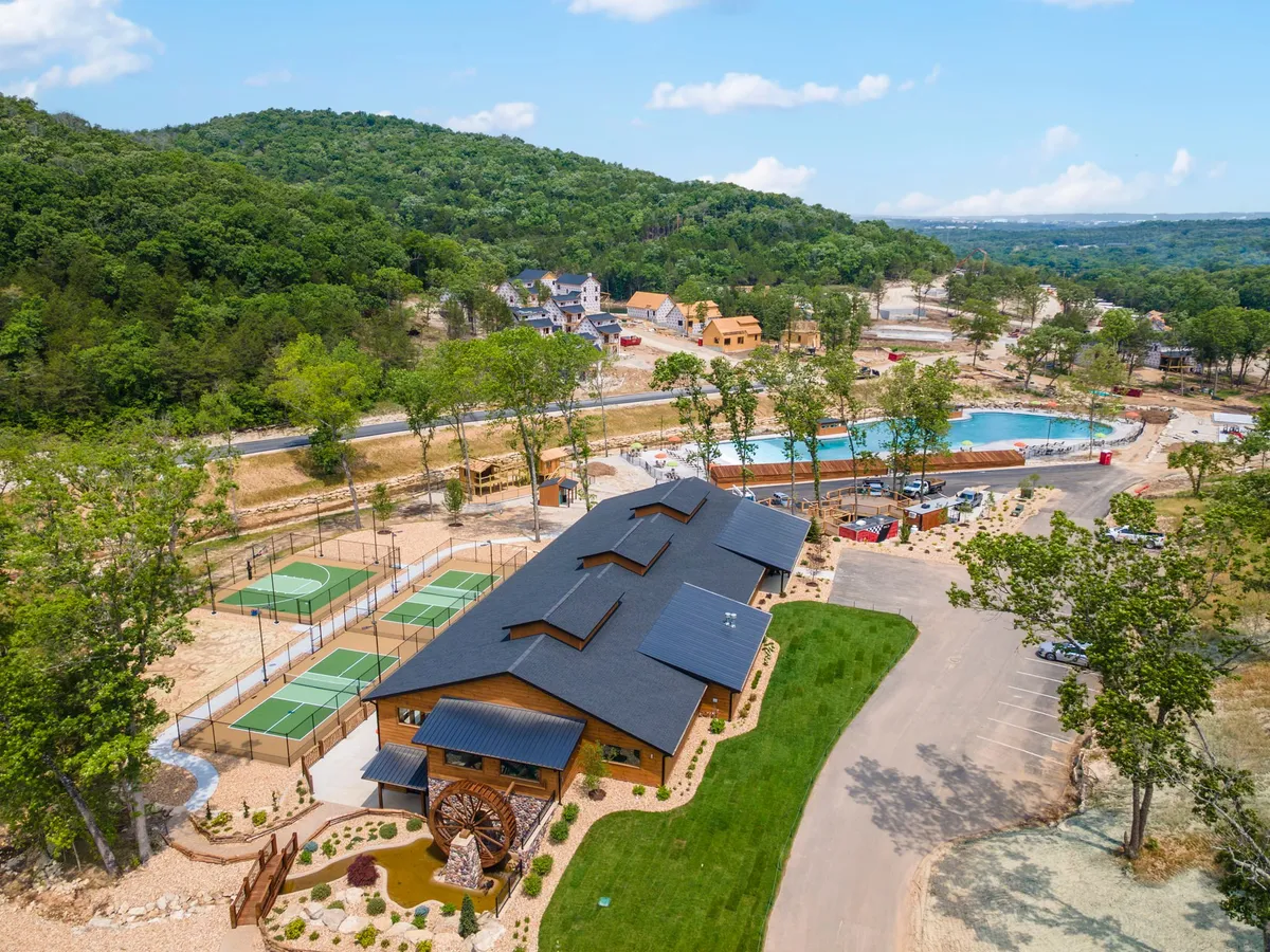 A view of the community center area featuring a swimming pool, tennis courts, and natural landscape in the background. The scene is energetic and communal, suggesting a range of shared activities and amenities for guests to enjoy as a group.
