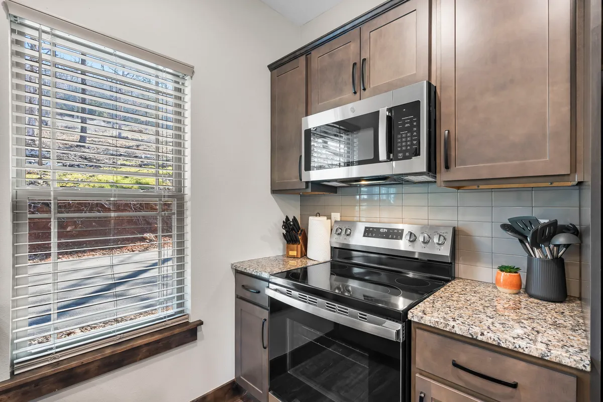 A welcoming kitchen scene with stainless steel appliances, a generous granite countertop, and a window that bathes the space in natural light. The countertop offers ample space for cooking or serving snacks.