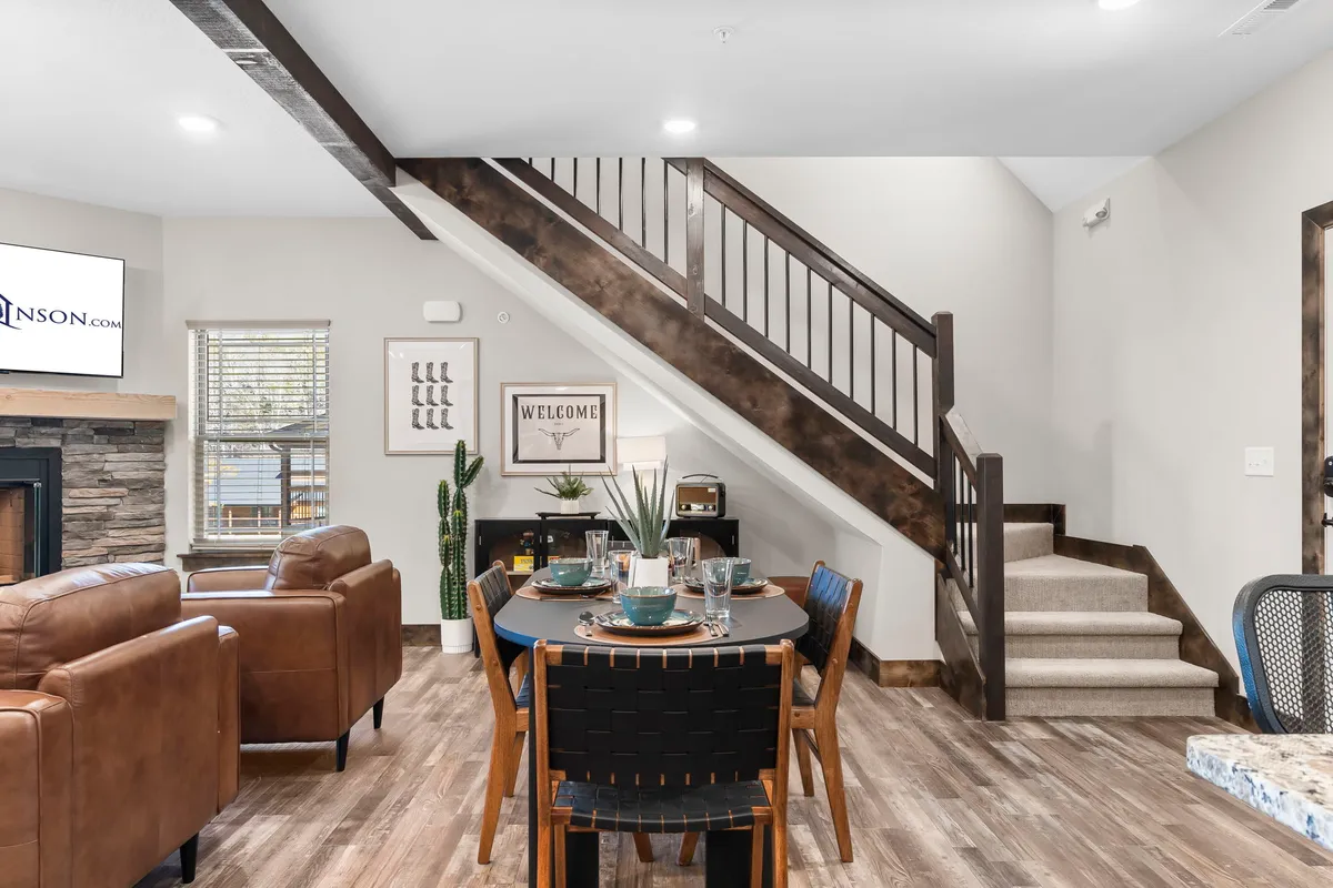 A dining area set for a meal, featuring a cozy table, comfortable leather couches, and a fireplace. The space is warm and inviting, with decorative touches and a staircase leading to the upper level.