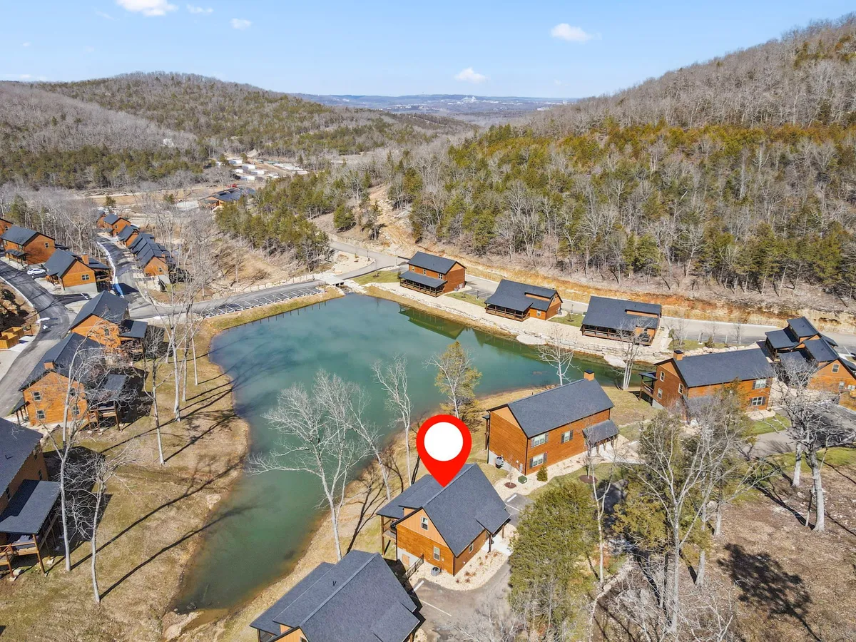 A tranquil view of lakeside cabins surrounded by trees, with a calm lake in the foreground. The scene is bathed in soft light, showcasing opportunities for fishing, hiking, and peaceful moments by the water.