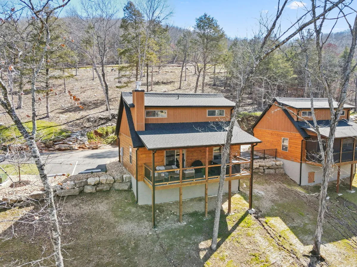 A tranquil exterior shot of a wooden cabin surrounded by tall trees, with a spacious deck area furnished for relaxation. The deck overlooks the natural setting, inviting you to step outside and enjoy peaceful mornings or sunset views amidst nature.